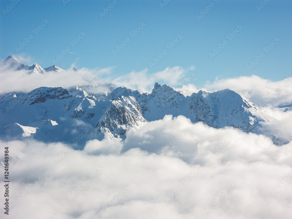 Fototapeta premium Low clouds leaving only the peaks of the snowy mountain tops visible in the winter on a sunny cold day with a clear blue sky