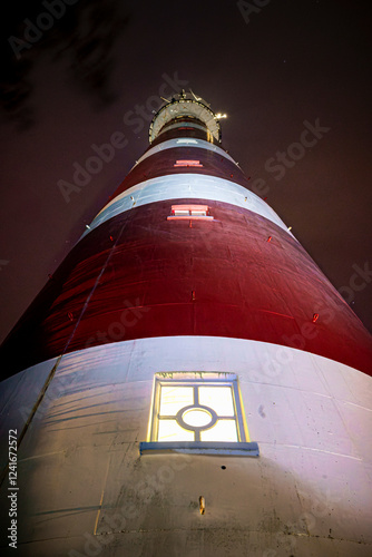 Majestic high up view of red with white striped lighthouse on Dutch Wadden Island at night time with stormy weather