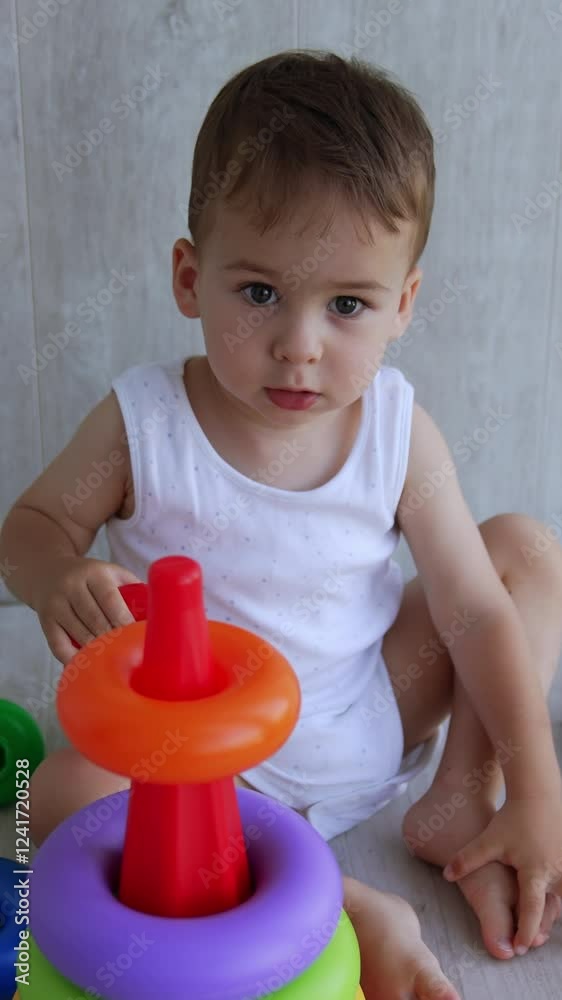 One year old toddler is busy assembling the pyramid. Baby puts the rings on the basis and then takes them off. High angle view. Vertical video One year old toddler is busy assembling the pyramid. Baby puts the rings on the basis and then takes them off. High angle view. Vertical video