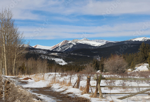 Snow-covered mountains and grassy meadow with rustic, wooden fence in the Rocky Mountains of Colorado