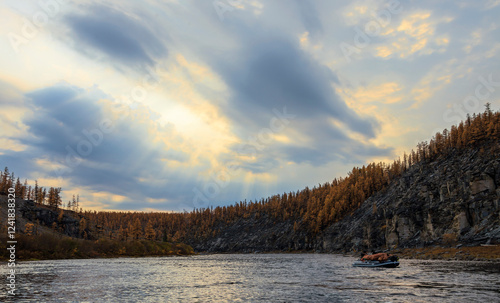Tourist boat and cloudy landscape with sunlight over the autumn taiga river.