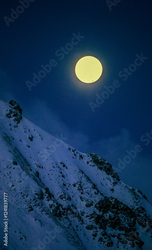 Celestial landscape with bright full disc-shaped moon above rocky mountainside.