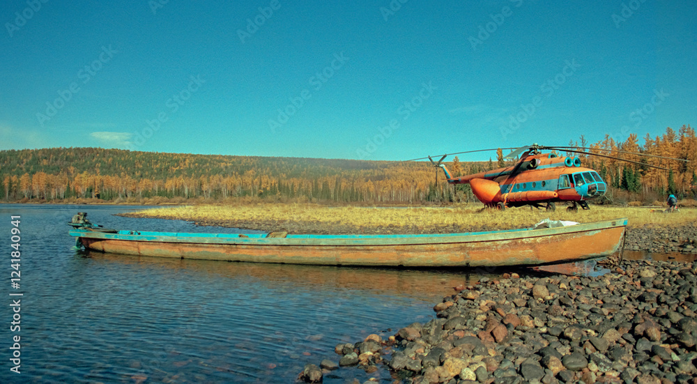 Obraz premium Homemade boat with an outboard motor and Soviet helicopter in upper reaches of Siberian river in autumn.