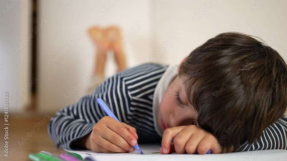 Young boy lying on floor, propped on one arm, drawing with blue pencil, feet playfully raised, immersed in creativity, concentration, and artistic exploration Young boy lying on floor, propped on one arm, drawing with blue pencil, feet playfully raised, immersed in creativity, concentration, and artistic exploration