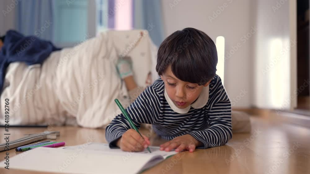 Young boy lying on the floor, drawing in a notebook with a green pencil, focused and creative in a peaceful indoor setting, capturing a moment of childhood imagination Young boy lying on the floor, drawing in a notebook with a green pencil, focused and creative in a peaceful indoor setting, capturing a moment of childhood imagination
