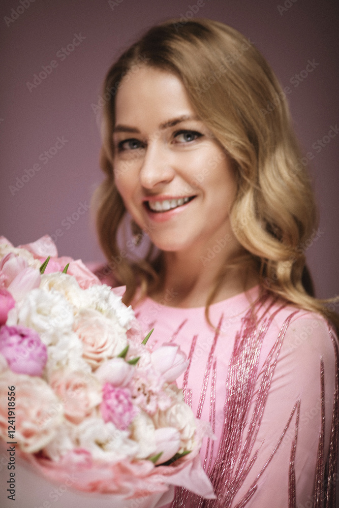 Blonde charming in a pink dress with flowers on a pink background, smiling happily, fashion and beauty, happiness, celebration Blonde charming in a pink dress with flowers on a pink background, smiling happily, fashion and beauty, happiness, celebration