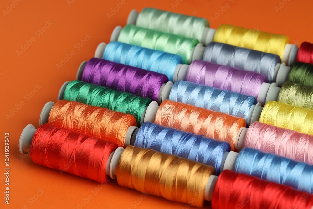 Different spools of sewing threads on orange background, closeup Different spools of sewing threads on orange background, closeup