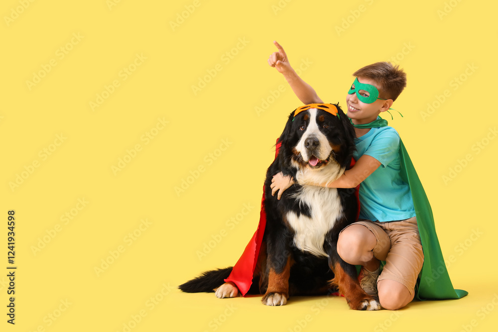 Cute fluffy dog and boy in superhero costumes pointing at something on yellow background Cute fluffy dog and boy in superhero costumes pointing at something on yellow background