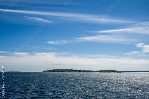 scenic view of a distant island under a vast blue sky with wispy clouds.