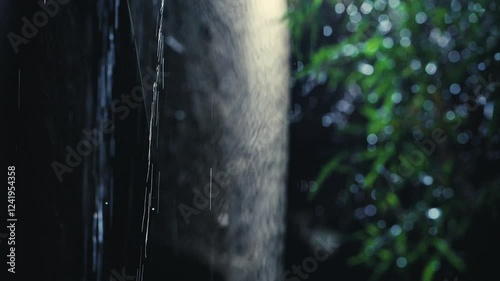 4K video of rain falling at night, illuminated by backlight. Raindrops visible against the dark background with audible rain sounds and occasional lightning strikes. photo