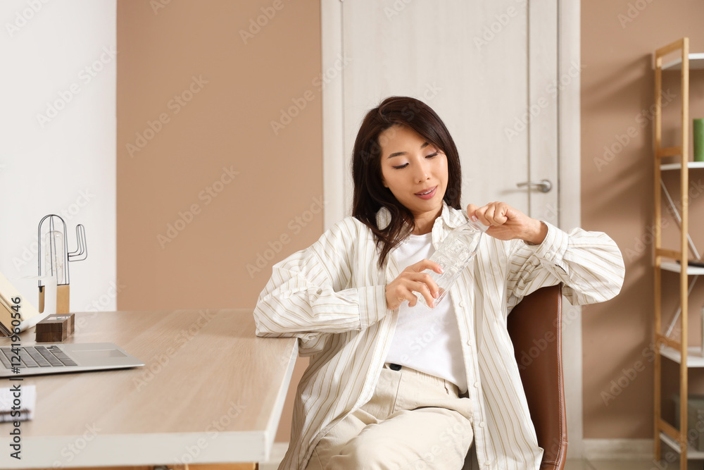 Young Asian woman opening bottle of water at table in office Young Asian woman opening bottle of water at table in office