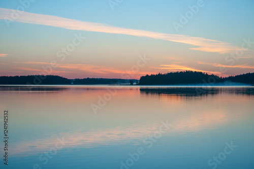 Early summer night by a calm lake in Finland with fog rising from the water
