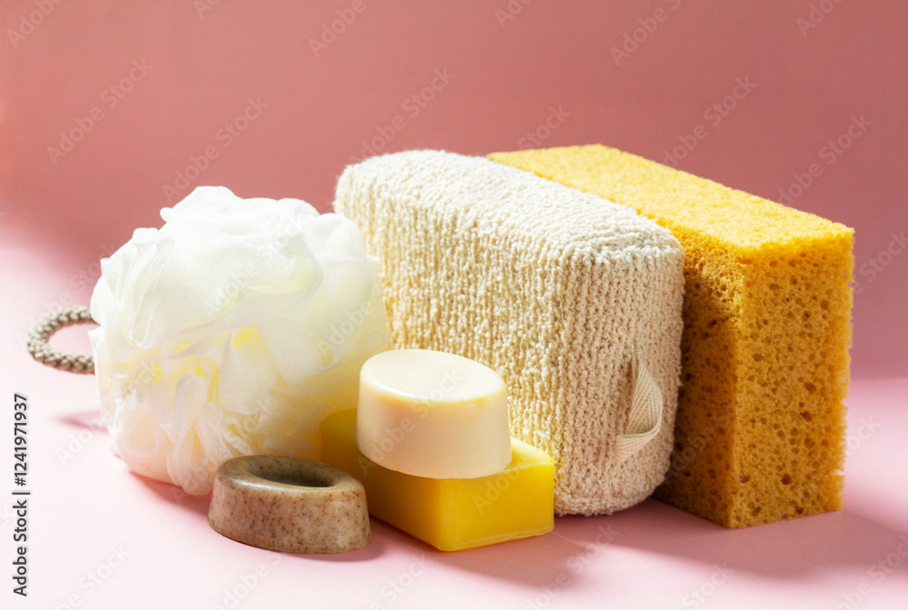 Set of bath accessories, sponges of different sizes and shapes and handmade soap on a pink background.