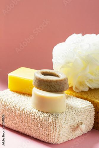 Set of bath accessories, sponges of different sizes and shapes and handmade soap on a pink background.
