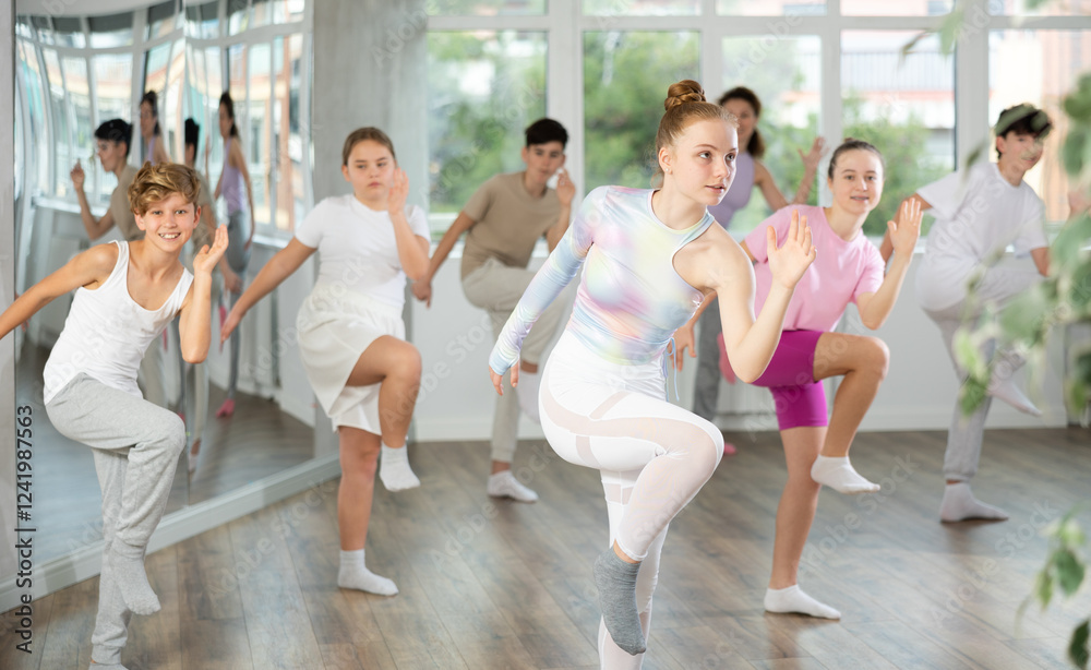 Naklejka premium Team of positive teenagers rehearsing modern dances in dance hall