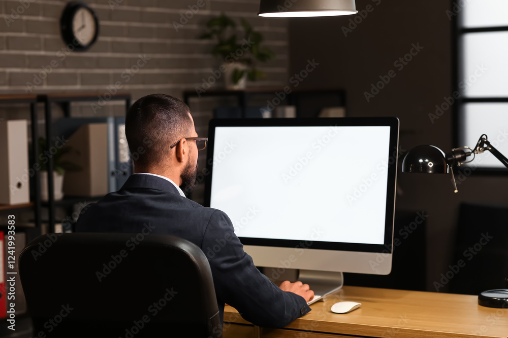 Young businessman working with blank computer on table in office at night, back view