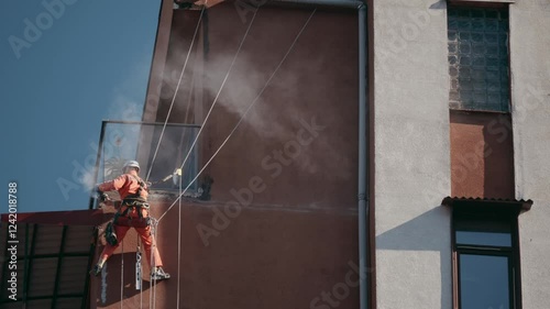 Industrial worker using angle grinder on high-rise building. Professional climber performing maintenance and repair work on facade, industrial profession concept. photo
