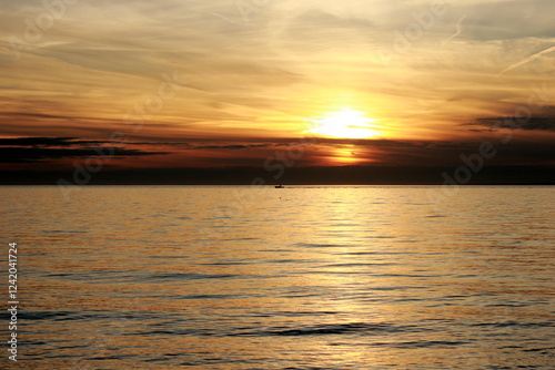 Boat traveling across water against bright orange sunset with dark clouds in Cape Cod, Connecticut 