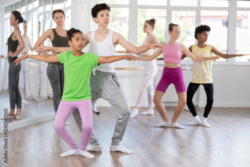 Slender teenage girl and boy practicing plie position of ballet during dancing courses