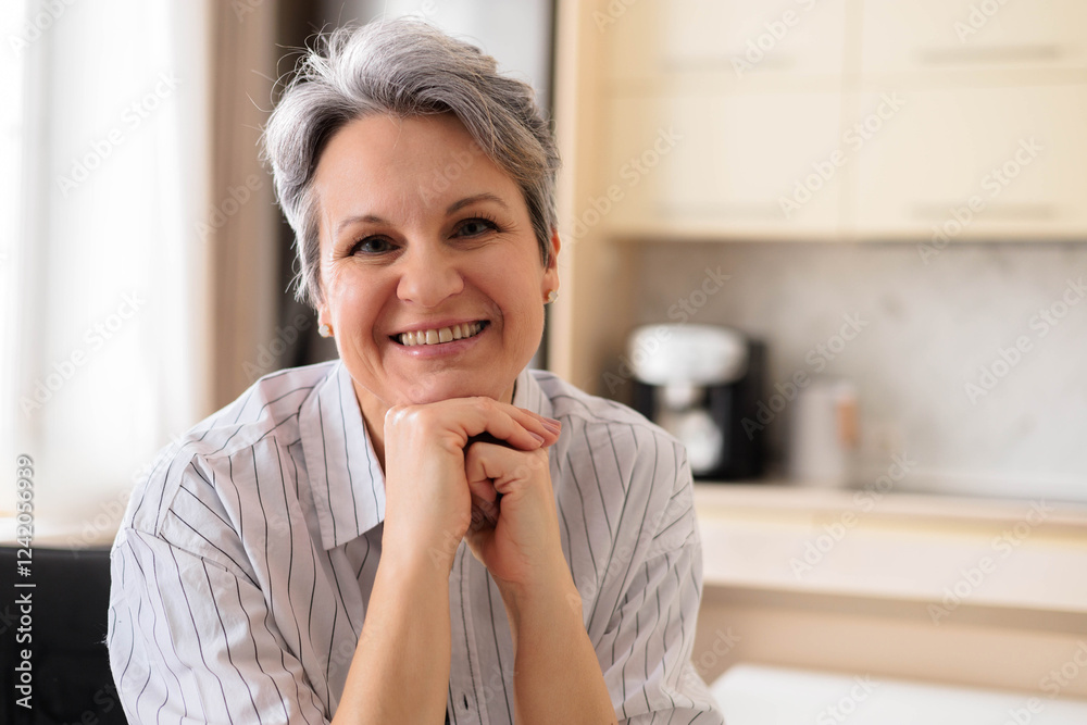 A beautiful elderly woman pensioner with gray hair sits at the table at home in her kitchen. A beautiful elderly woman pensioner with gray hair sits at the table at home in her kitchen.