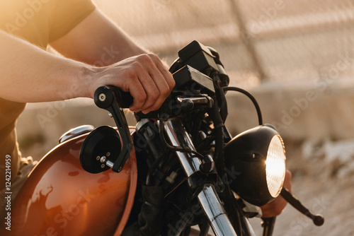 Biker holding handlebars of a custom motorcycle at sunset photo