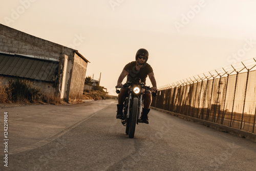 Biker riding custom motorcycle on empty road at sunset