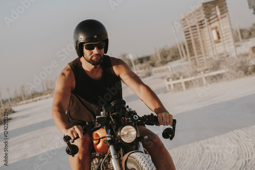 Biker riding custom motorcycle on sandy road near beach hut photo