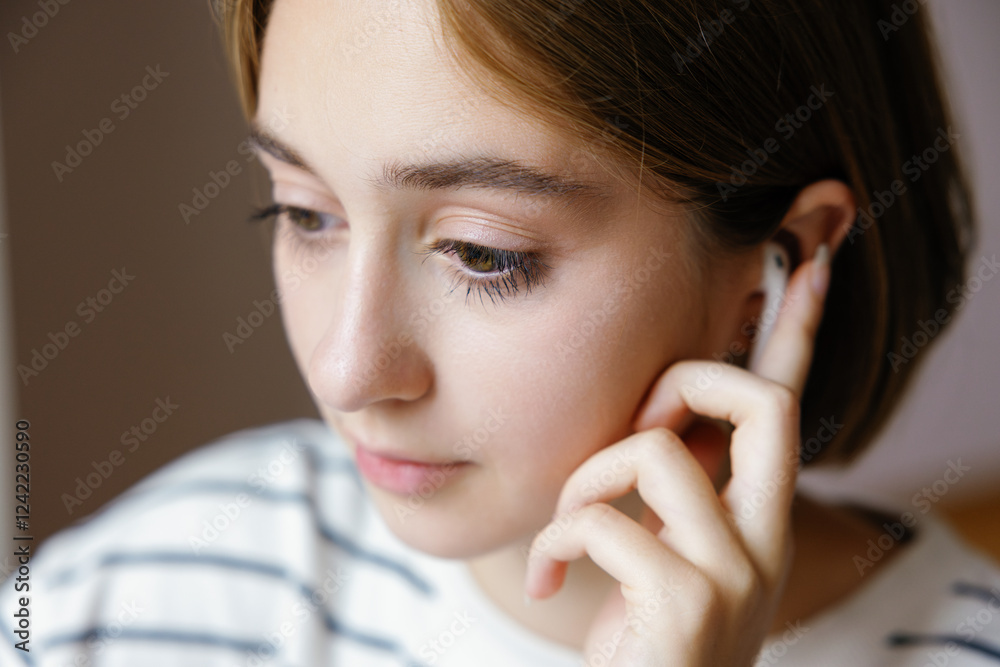 Close up facial of cropped girl pushing on earphone at blurred home Close up facial of cropped girl pushing on earphone at blurred home