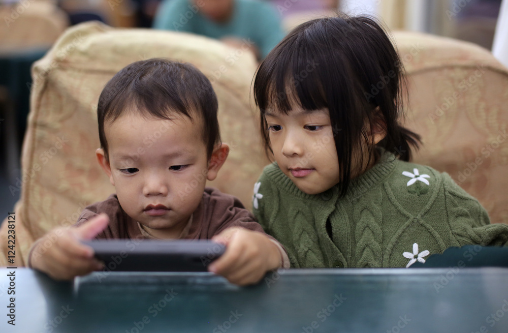 Asian brother and sister playing with their phones on the train seats Asian brother and sister playing with their phones on the train seats