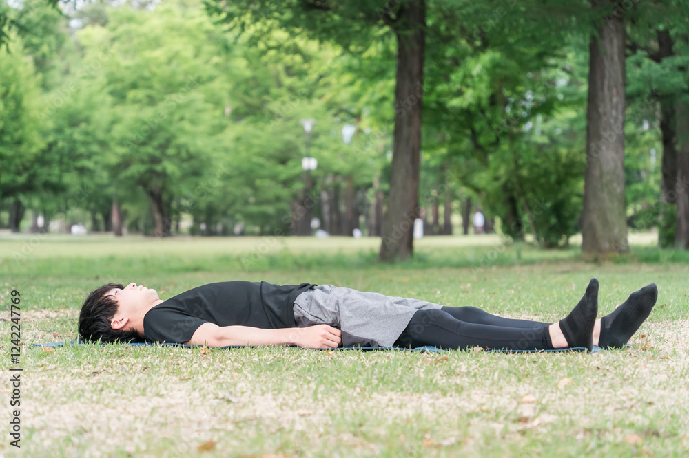 Fototapeta premium 公園でヨガマットをひいてヨガ・ピラティスをする若い男性