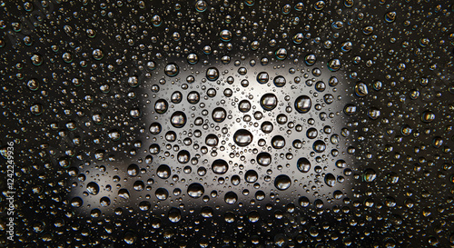Close-up perpendicular shot of a water droplet-covered glass surface, with light refractions creating a unique texture
