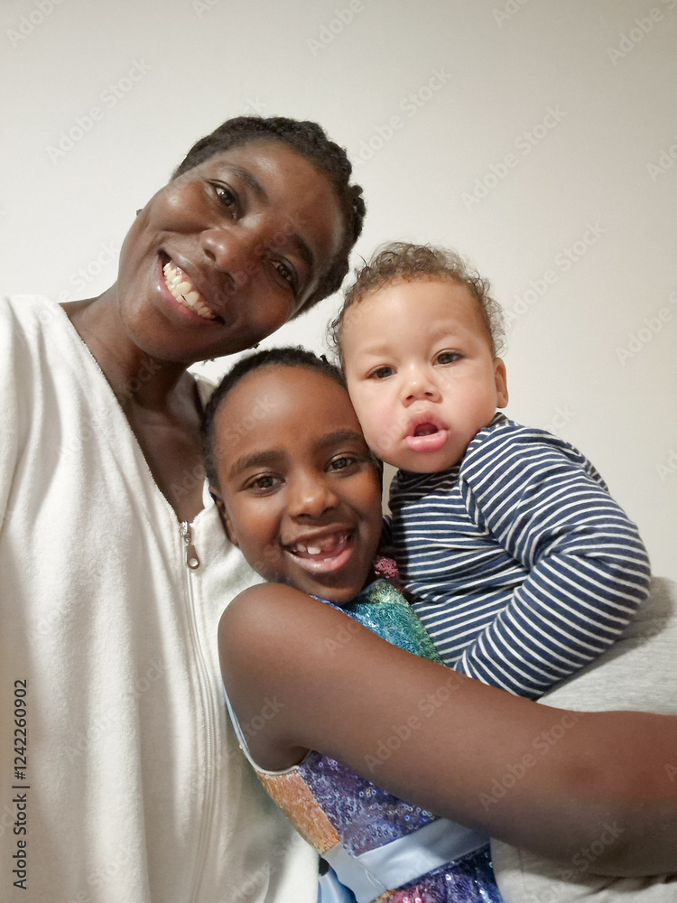 Older Sibling Holding Baby Brother with Mother Standing by Wall Older Sibling Holding Baby Brother with Mother Standing by Wall