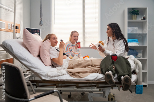 Teenage friends visiting and eating with patient in hospital bed photo