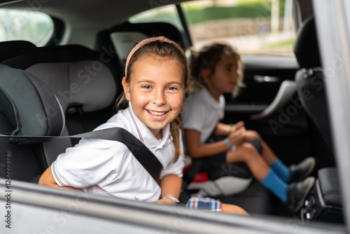 Happy schoolgirl wearing seat belt sitting in car going to school photo