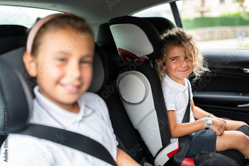 Two smiling school students sitting in booster seats inside car