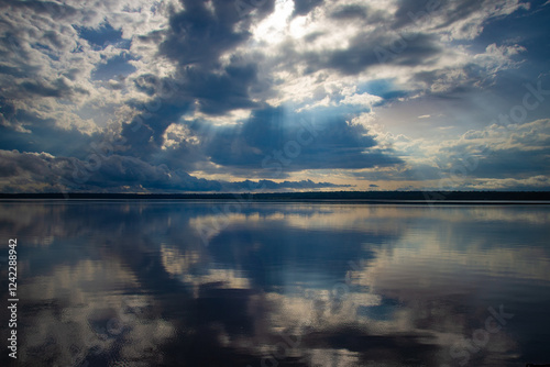 Dramatic cloudy sky with sun rays over a calm river, reflecting clouds. photo