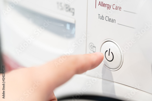 A finger pressing the start button on a washing machine. Close up view of automatic washing machine.