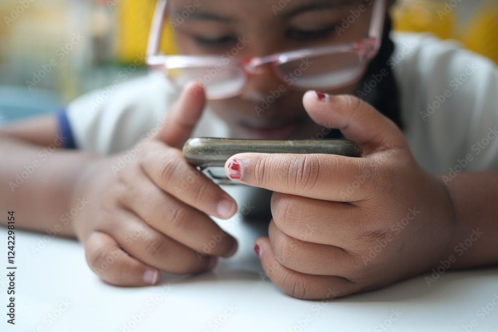 Obraz premium Child focused on smartphone while sitting indoors