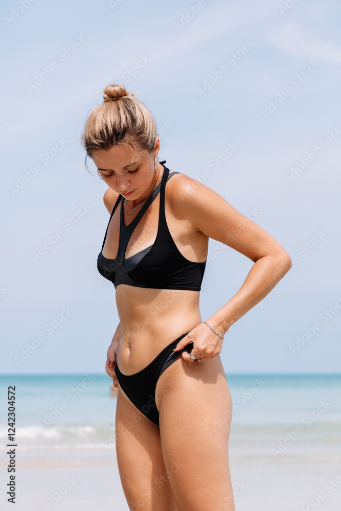 Woman adjusting her black bikini on a sunny beach Woman adjusting her black bikini on a sunny beach