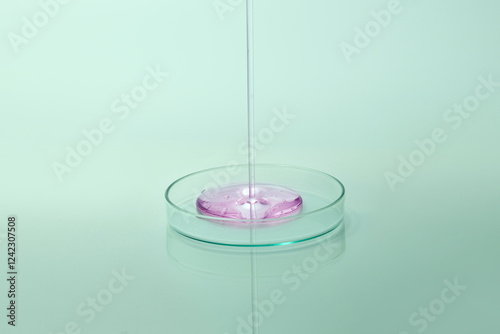 A stream of transparent liquid is poured into a glass petri dish photo