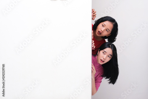 Two girls peeking from behind a wall showing funny shocked face expression photo