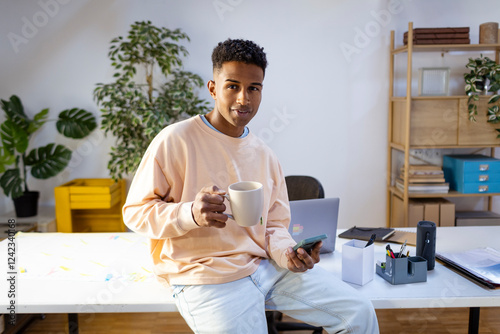 Portrait of young man drinking tea and checking smartphone in office photo