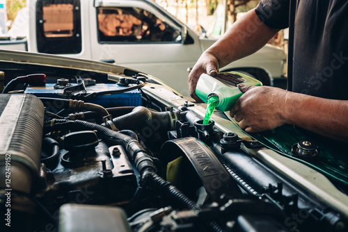 Male professional mechanic pouring antifreeze coolant liquid into car engine radiator in service center. Concept of car radiator coolant maintenance