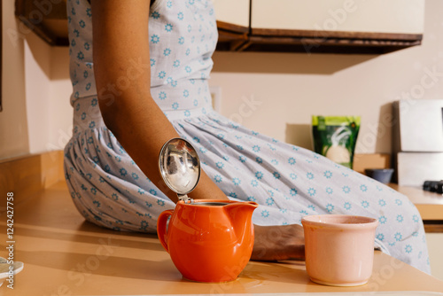 Anonymous Woman sitting next to teapot and cup on kitchen counter photo