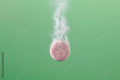 A Pink Tablet Dissolving in Water on Green Background