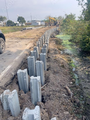 I-shaped concrete piles in the ground, two rows of piles, along the canal, cars and backhoes, workers, dam construction