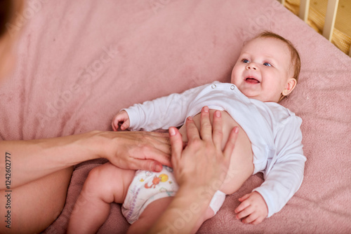 Valokuva Young mother applies cream to baby girl lying on soft pink blanket