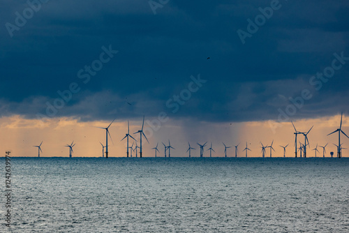 Dark clouds of a thunderstorm with rain falling onto the north sea with silhouettes of wind turbines in the background