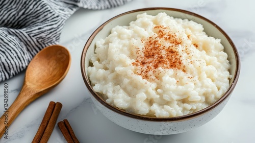 A bowl of creamy rice pudding topped with a sprinkle of spice, served with a wooden spoon.
