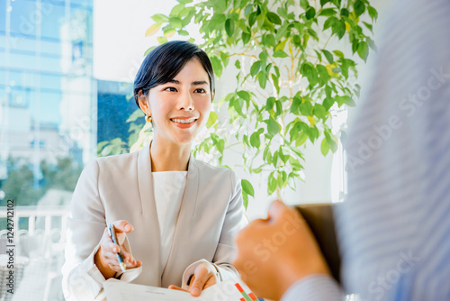 明るい室内で顧客にプレゼンテーション資料の説明をして営業する30代の笑顔の女性